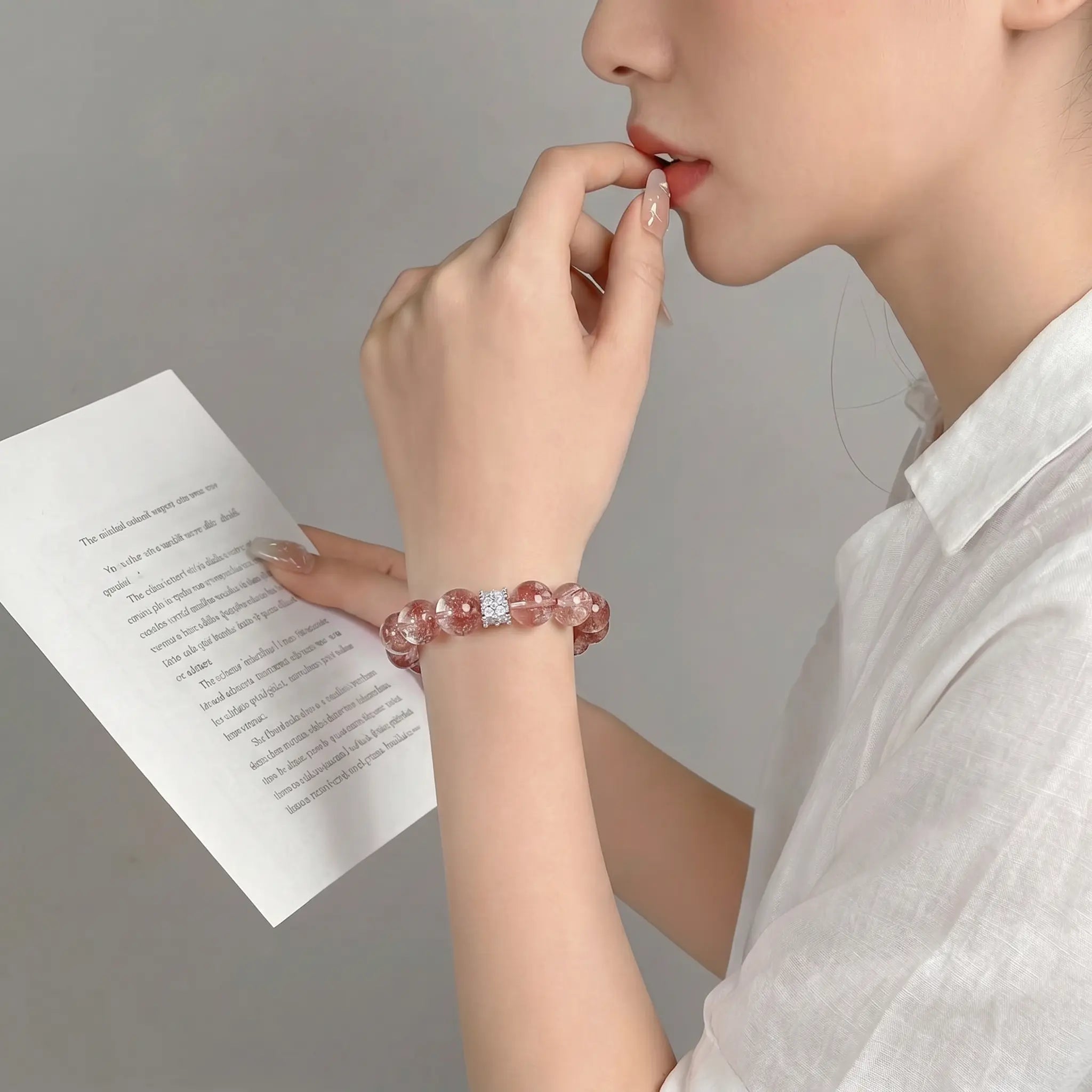 Left profile close-up of an elegant woman touching her lips in a thinking pose revealing a pink gemstone bracelet.