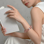 Left-side perspective detail shot of a woman hands holding a book displaying a natural mineral crystal wrist bracelet.