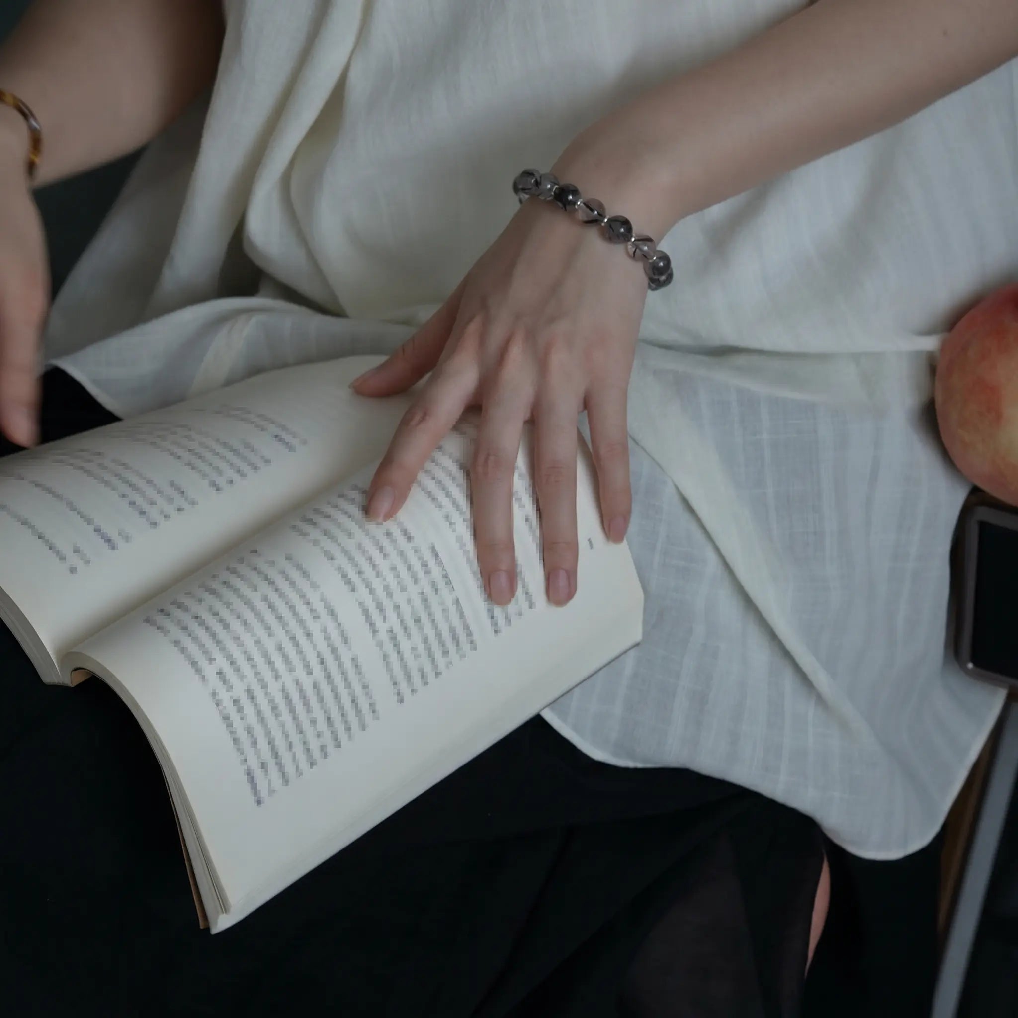 Left profile close-up from lower body to knees showing an elegant seated lady holding a book on her lap with a gemstone bracelet.