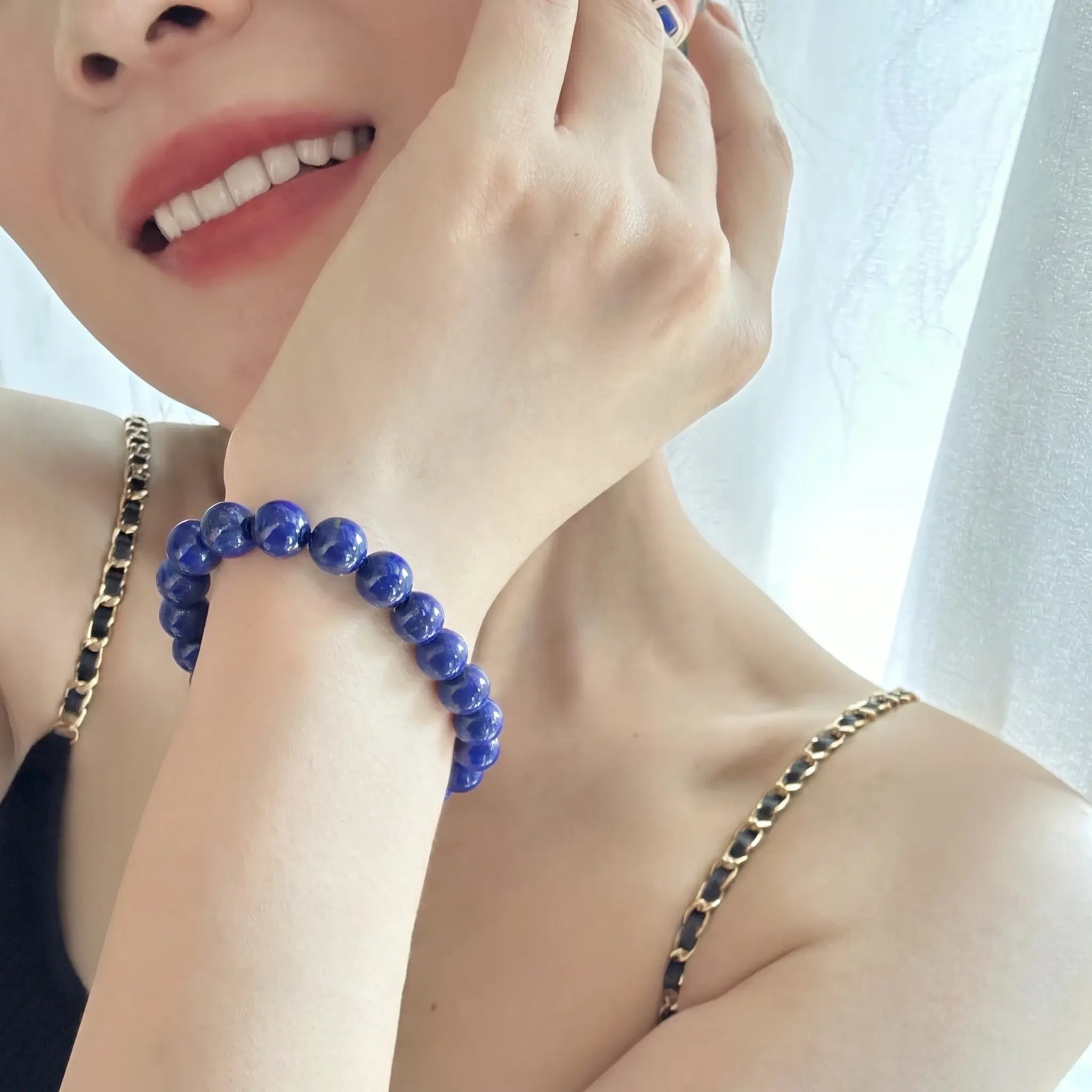 Close-up shot of a smiling woman displaying the Celestial Lapis Bracelet resting against her cheek in soft morning sunlight.