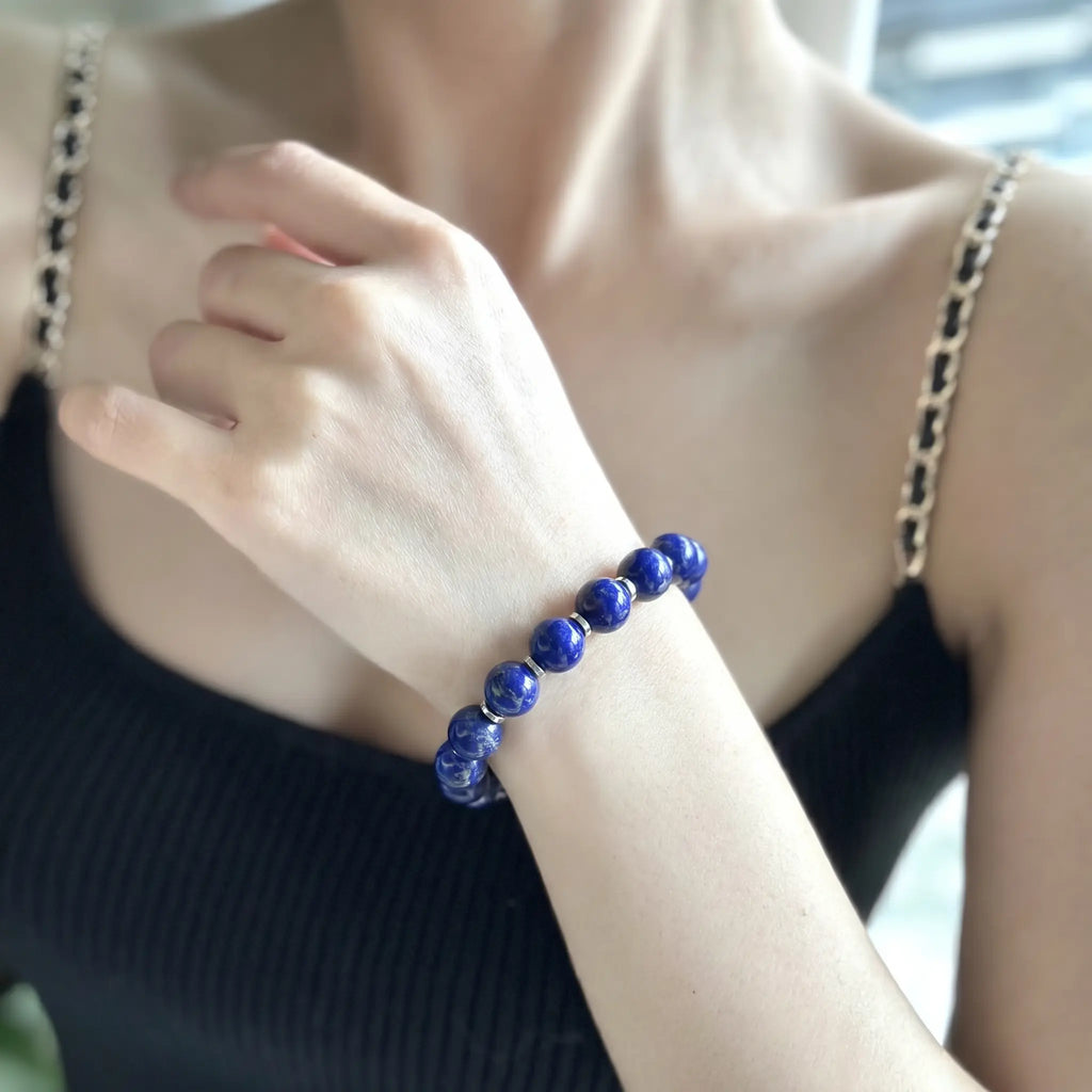 Front close-up view from collarbone to chest of a woman wearing the Celestial Lapis Bracelet on her arm styled with a black chain-strap top.