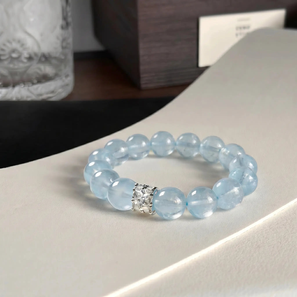 The coastal elegance aquamarine bracelet displayed elegantly flat on a curved white surface near a vintage glass cup.