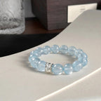 The coastal elegance aquamarine bracelet displayed elegantly flat on a curved white surface near a vintage glass cup.