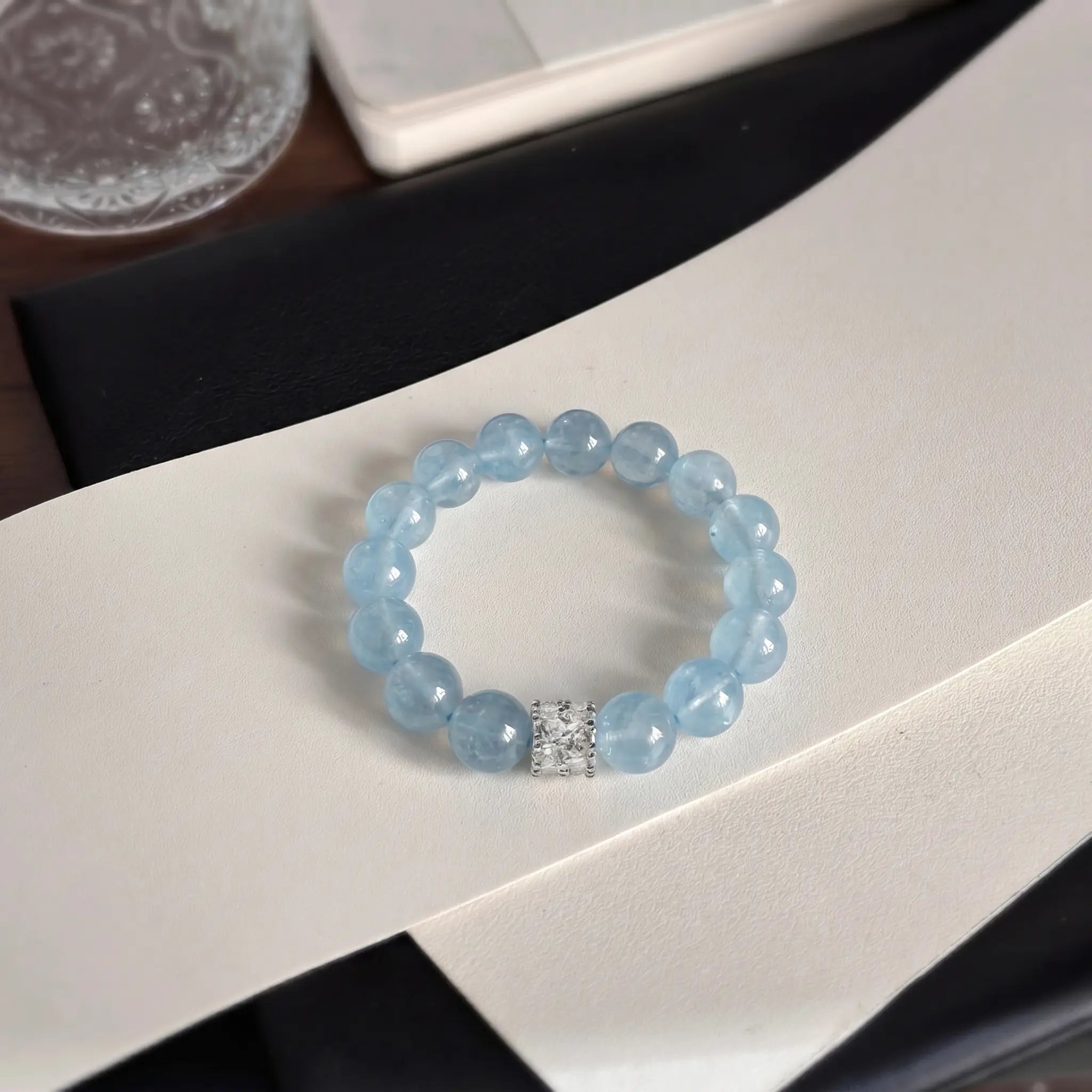 Top-down high angle shot of the coastal elegance aquamarine bracelet centered over a curved white display surface.