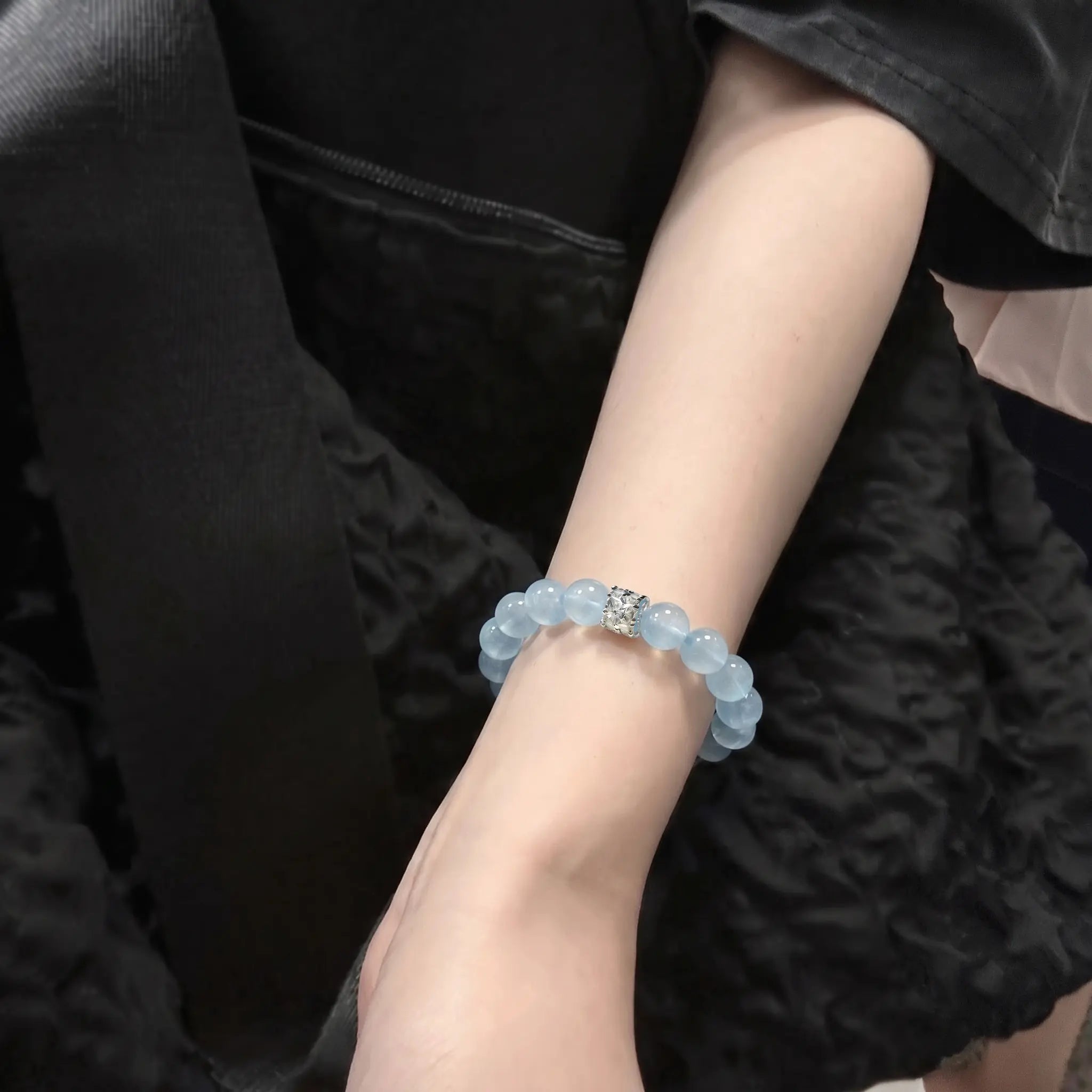 Close-up shot of the coastal elegance aquamarine bracelet adorned on a woman wrist against dark textured clothing.