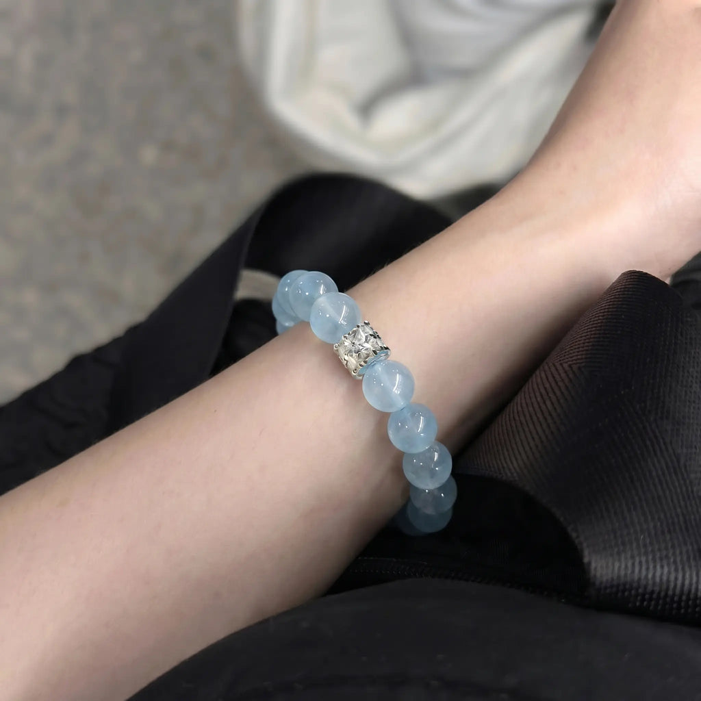 Close-up shot of the coastal elegance aquamarine bracelet worn on a left wrist extended diagonally across dark pinstripe clothing.