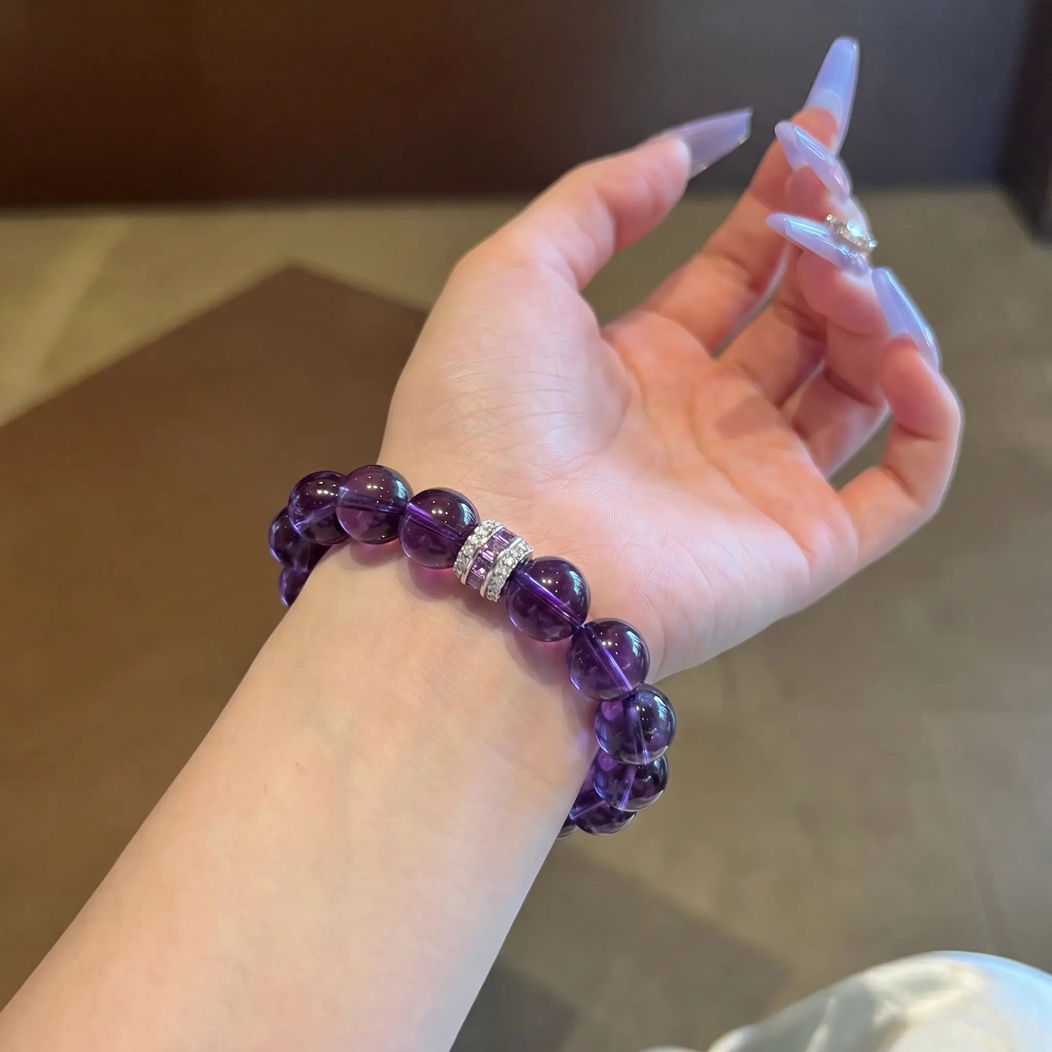 First-person POV view of a woman open palm upward displaying the Eternal Elegant Amethyst Bracelet under warm indoor light.