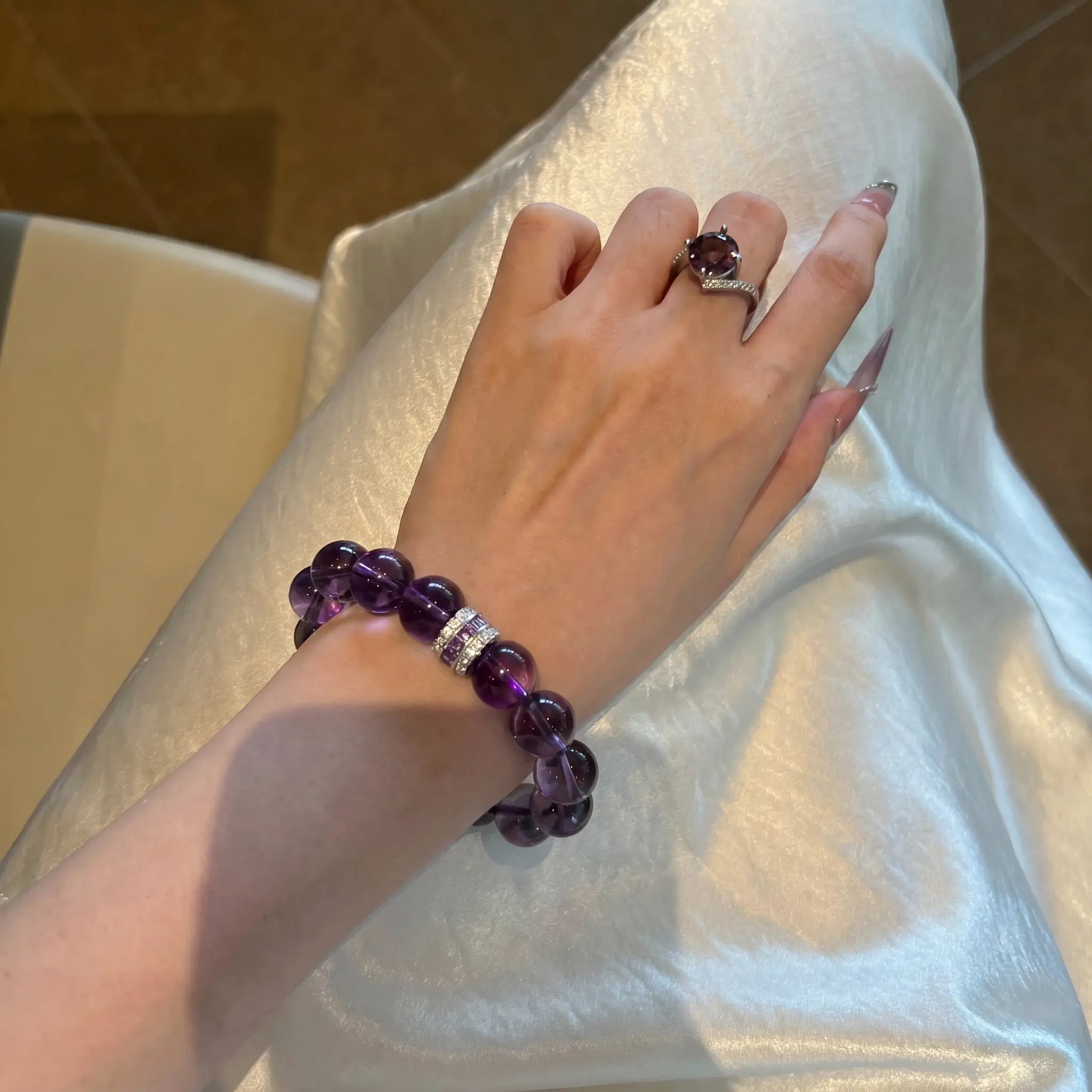 Close-up portrait view of a female wrist wearing the Eternal Elegant Amethyst Bracelet resting over shining white silk fabric.