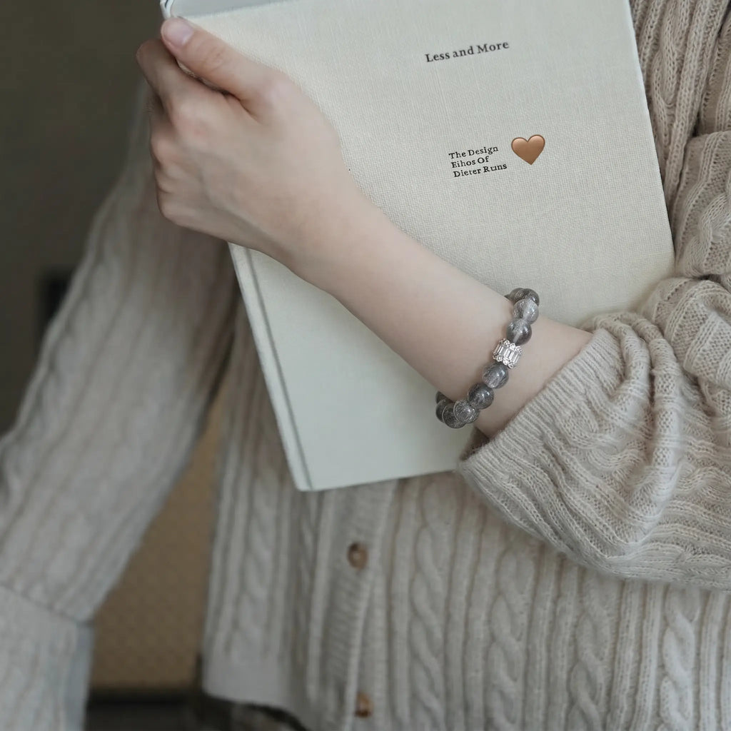 Left-side perspective of a woman clutching a hardcover book to her chest revealing a clear quartz crystal bracelet.