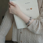 Left-side perspective of a woman clutching a hardcover book to her chest revealing a clear quartz crystal bracelet.
