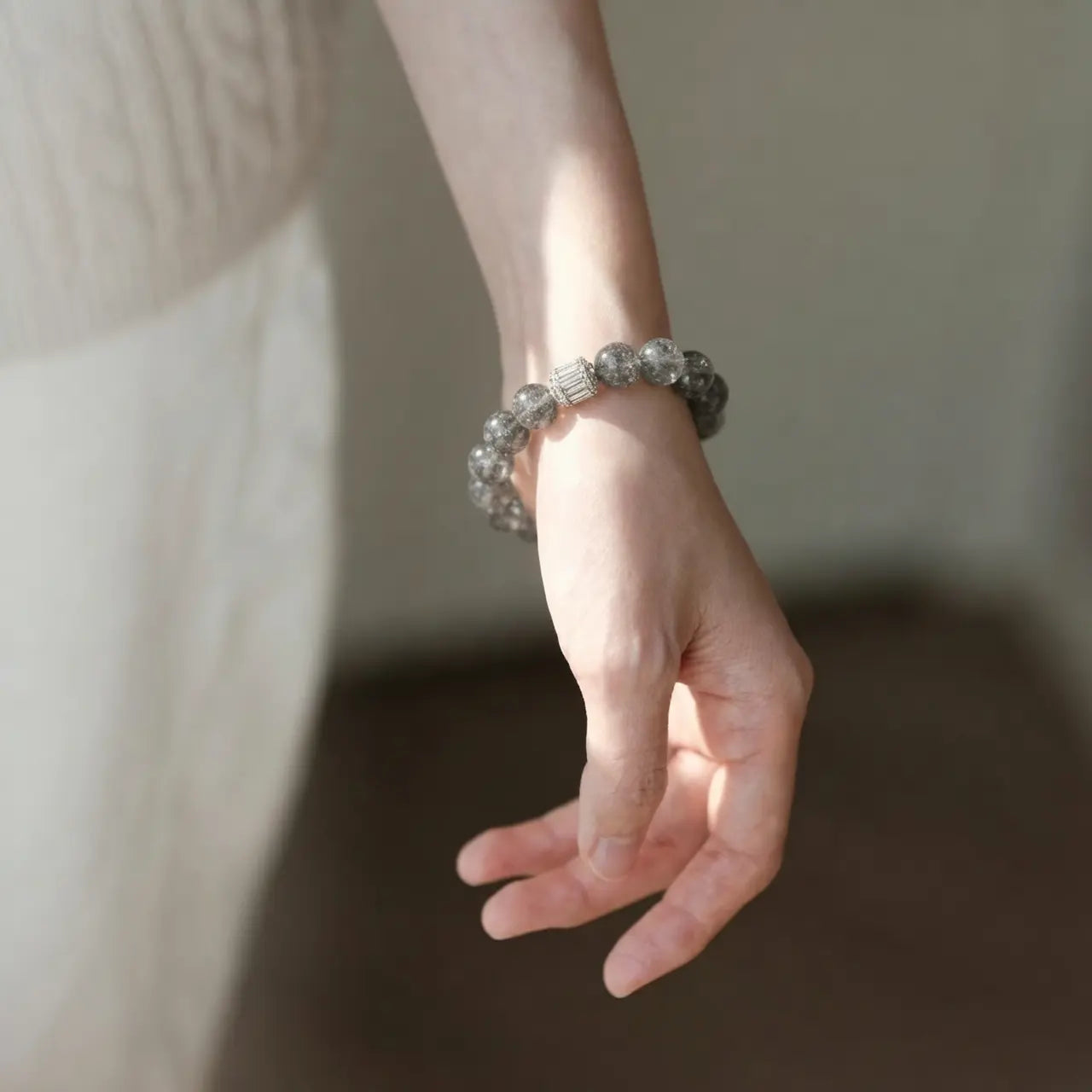 Front close-up view of a woman left arm resting naturally downward showcasing the clear quartz beaded bracelet.