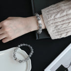 Top-down high angle shot showing a female left wrist resting flat over a clean desk surface with a clear mineral bracelet.