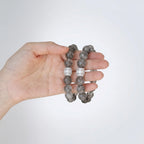 Close-up shot of a single left hand holding two layered clear crystal quartz bracelets against a plain white backdrop.