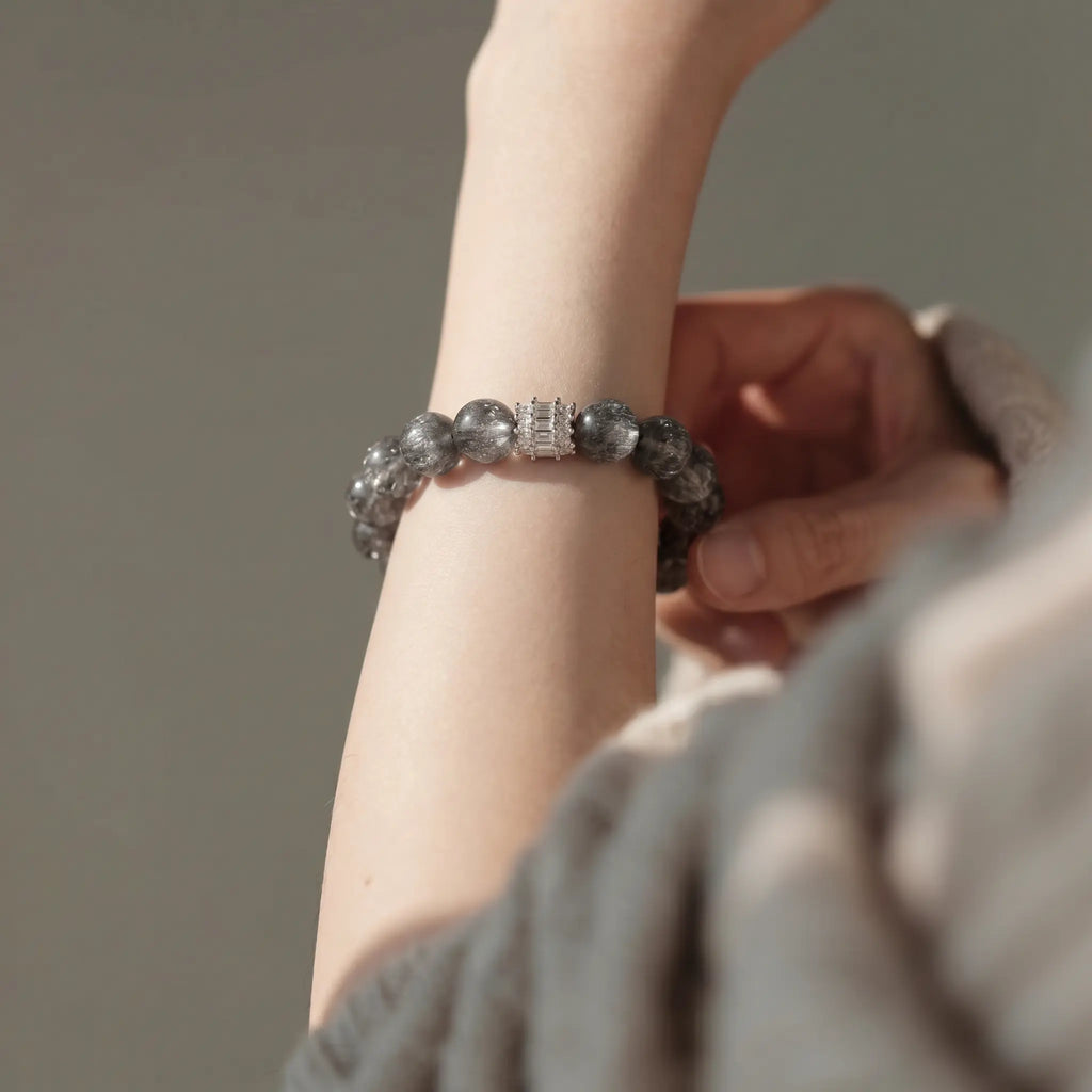 Over-the-shoulder shot focusing on right fingers adjusting a clear quartz bracelet on a raised left wrist.