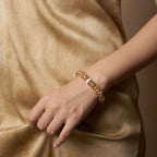 Front close-up of a woman left hand elegantly pinching her skirt at the abdomen to showcase a hematoid quartz bracelet.