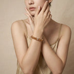 Cropped portrait to the nose showing a woman with crossed arms gently caressing her chin with a gemstone wrist bracelet.