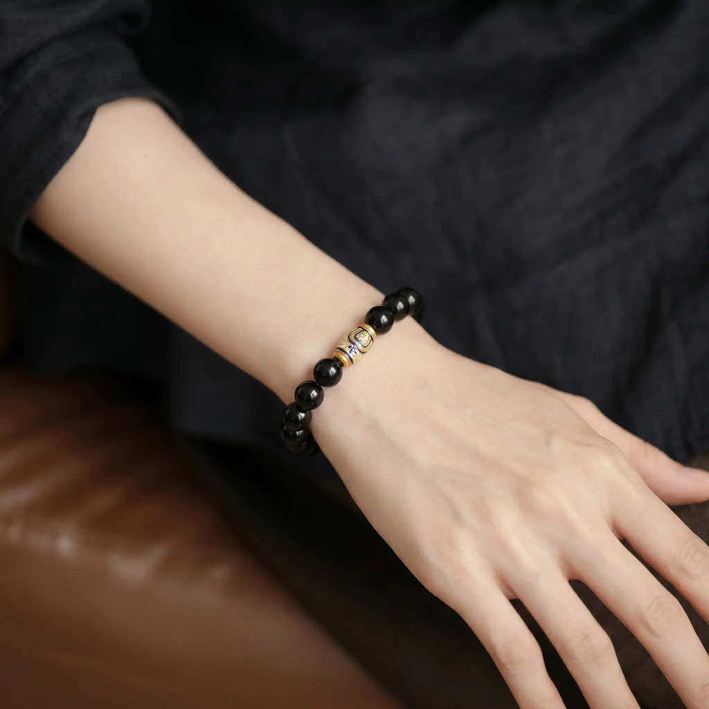 Diagonal perspective from top-left to bottom-right showing a woman arm resting on a cozy sofa with an obsidian bracelet.