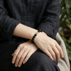 Detailed view of a woman with crossed legs and hands folded over knees revealing an artisan enameled obsidian bracelet.