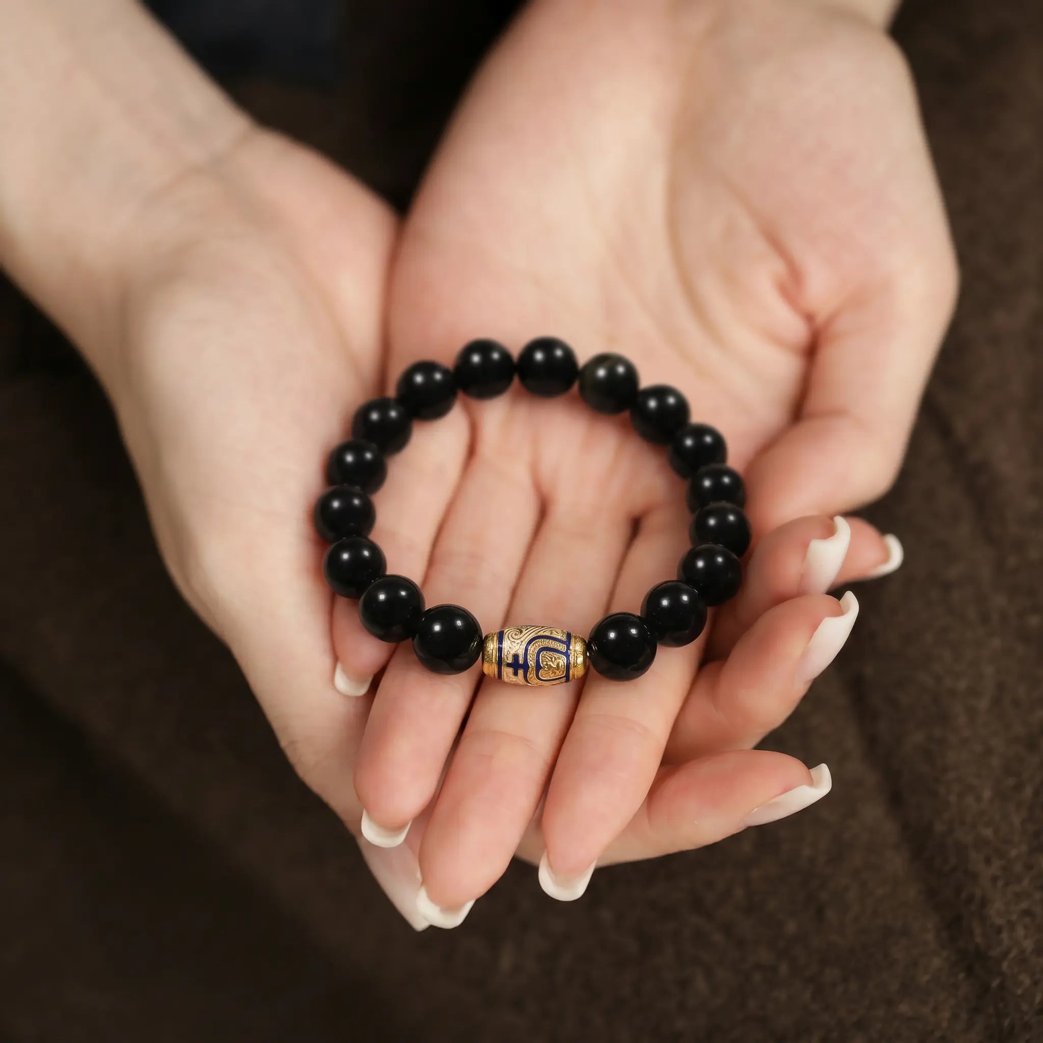 Macro shot of a left hand resting over a right open palm cradling the fine enameled gemstone bracelet.