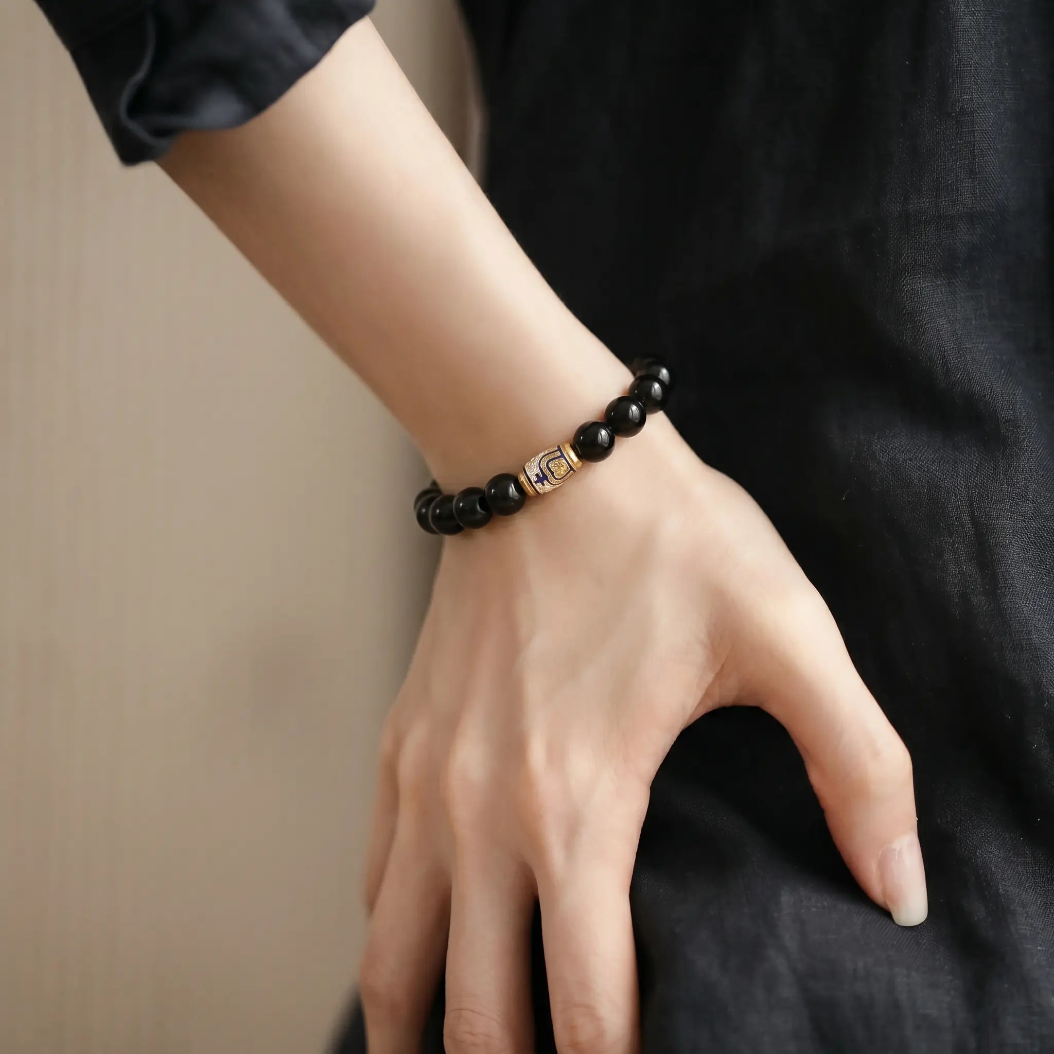A hands-on-hip pose close-up highlighting a luxury black obsidian gemstone bracelet on a woman styled wrist.