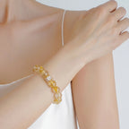Front view close-up of a right hand resting on the opposite left shoulder revealing a yellow gemstone bracelet.