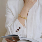 Front portrait of a woman with a book on her lap while her right hand touches the chin in a thinking pose showing the quartz bracelet.