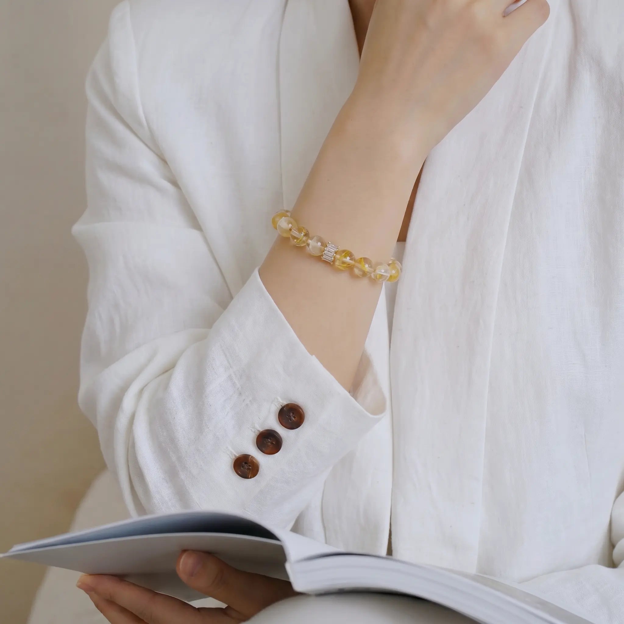 Front portrait of a woman with a book on her lap while her right hand touches the chin in a thinking pose showing the quartz bracelet.