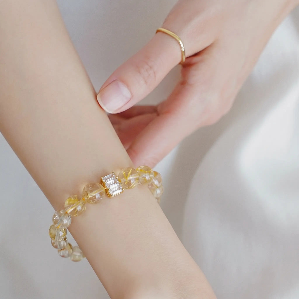 Detailed perspective of a left hand gently touching the right wrist styled with a golden quartz crystal bracelet.