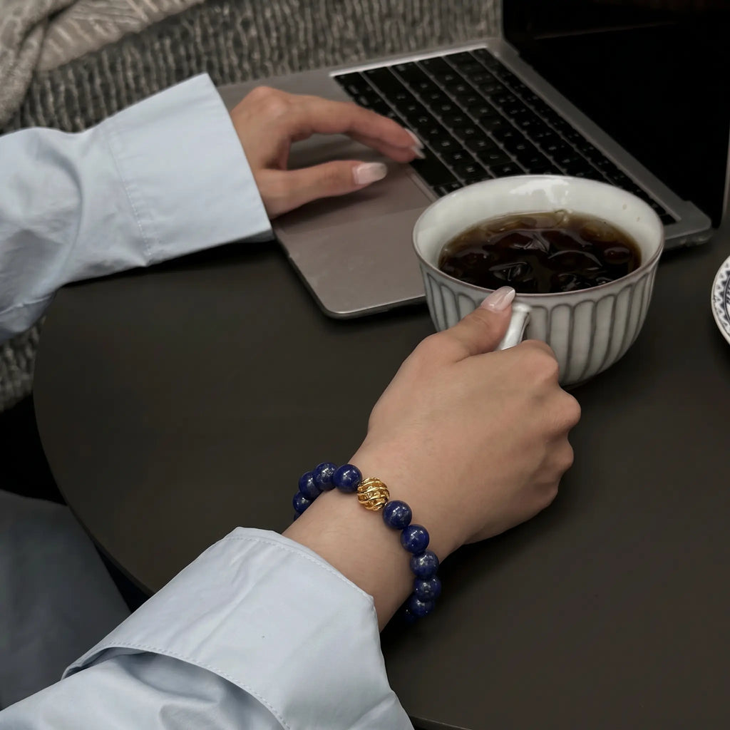 Close-up shot of hands on a desk with the right wrist holding a coffee cup while the left hand is typing on a laptop keyboard.