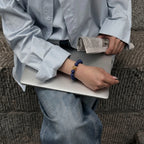 Top-down upper body shot of a woman with crossed legs, her right hand resting flat on a laptop while her left hand holds a printed newspaper.