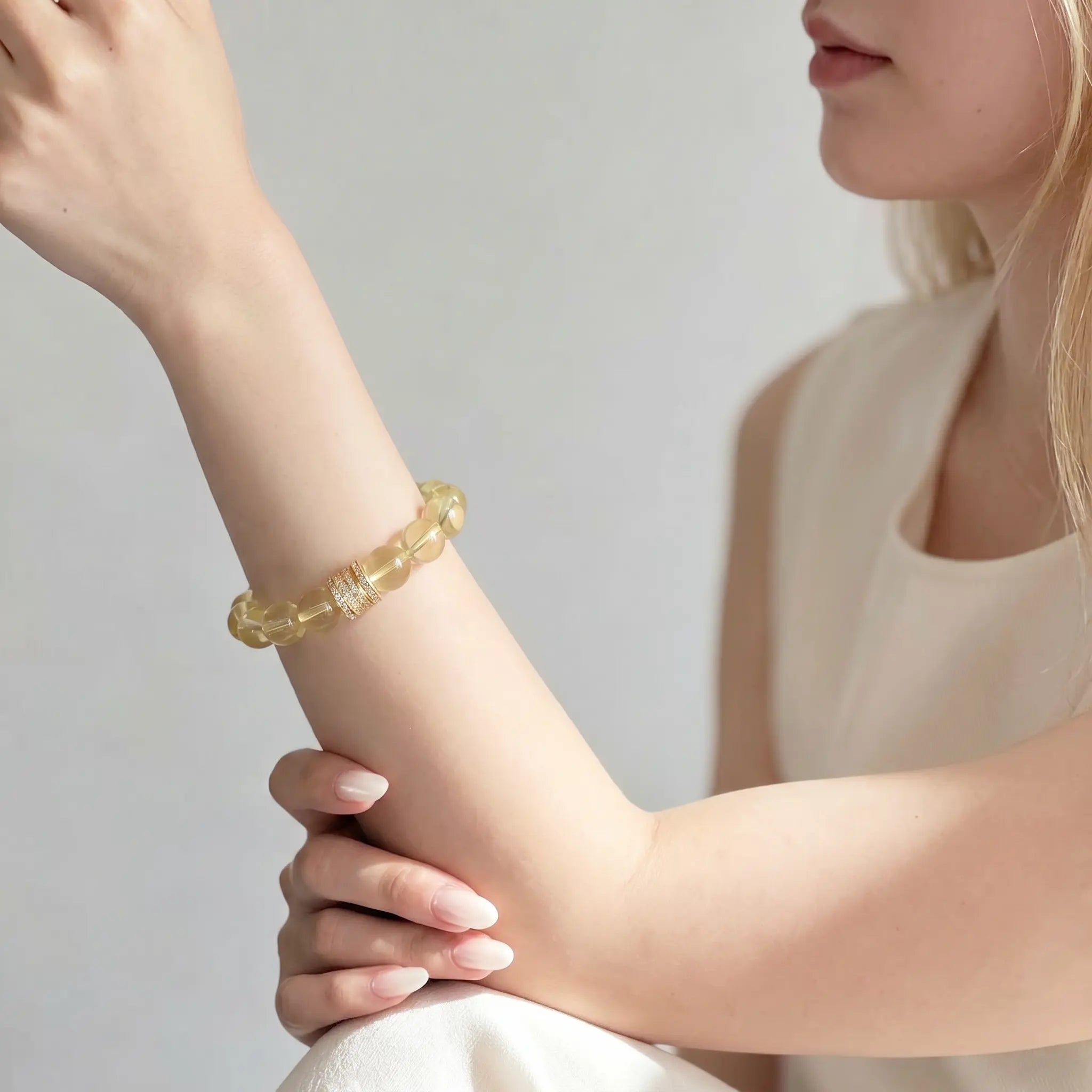 Left-side profile close-up of a woman raised left hand resting over her thigh showcasing the golden aura crystal bracelet.