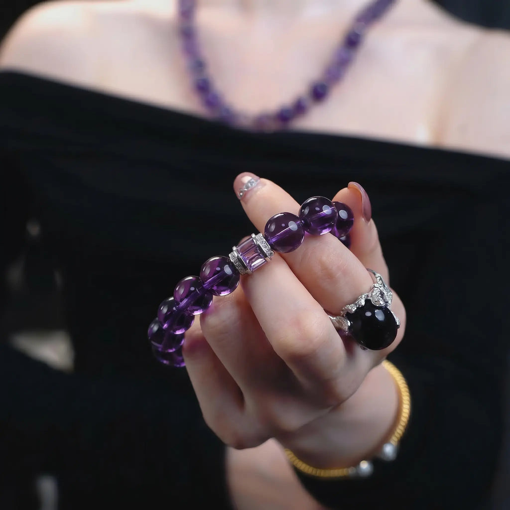 Close-up shot of a woman hand in a pinching gesture displaying the graceful amethyst poise bracelet crystal against her black off-the-shoulder top.