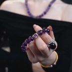 Close-up shot of a woman hand in a pinching gesture displaying the graceful amethyst poise bracelet crystal against her black off-the-shoulder top.