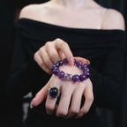 Close-up view of overlapping hands presenting the graceful amethyst poise bracelet crystal against a black off-the-shoulder top.