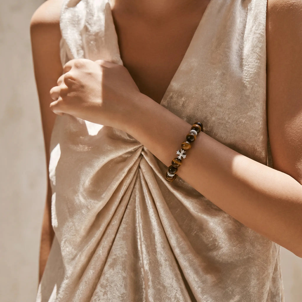 Front portrait crop from abdomen to shoulder showing a female left hand presenting a tiger's eye bracelet against her clothing.