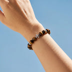 A wrist adorned with a gemstone cross bracelet reaching toward the sky from a lower-right to upper-left angle.