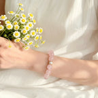Right-side profile close-up of a woman left wrist holding a fresh chrysanthemum flower with her pink crystal bracelet.