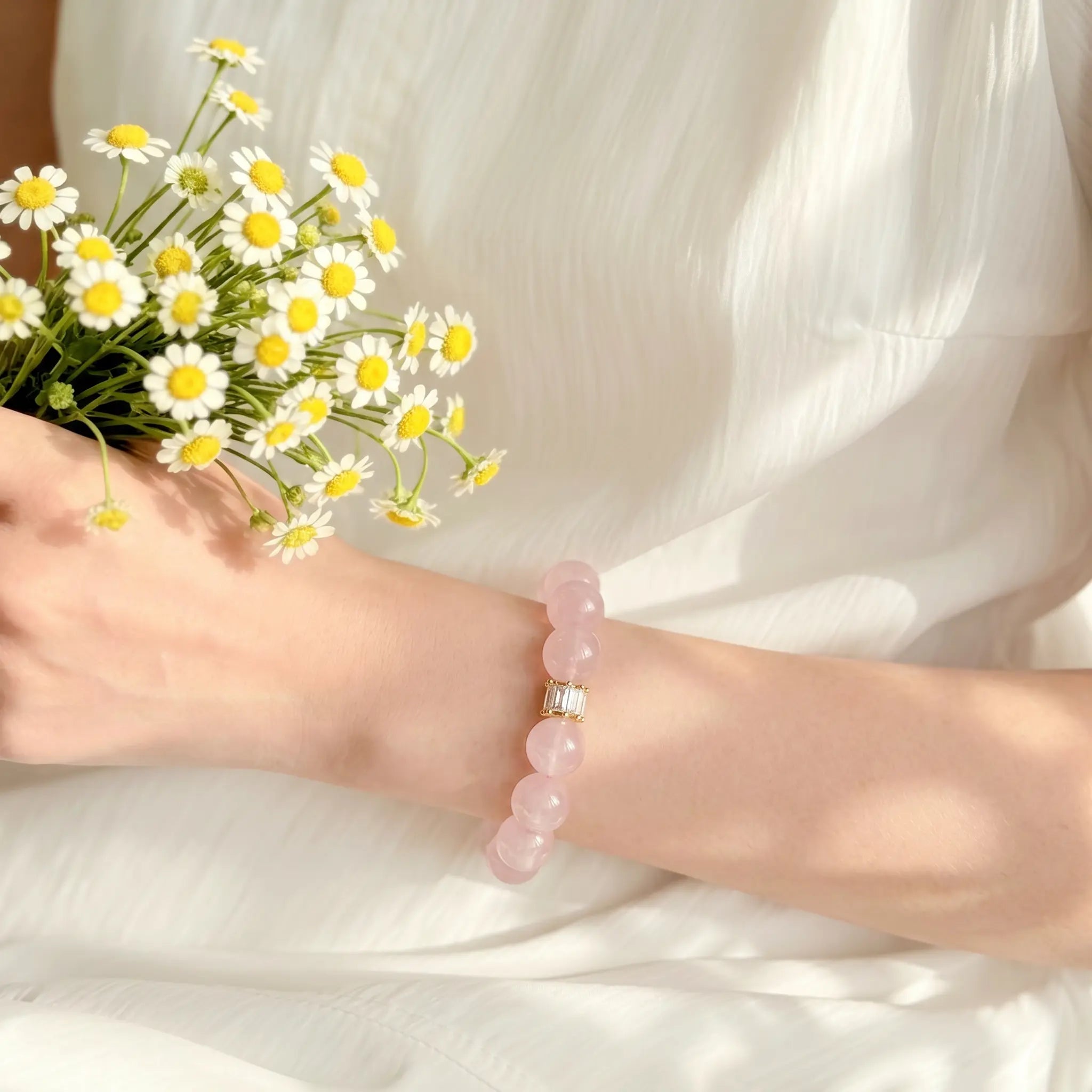 Right-side profile close-up of a woman left wrist holding a fresh chrysanthemum flower with her pink crystal bracelet.