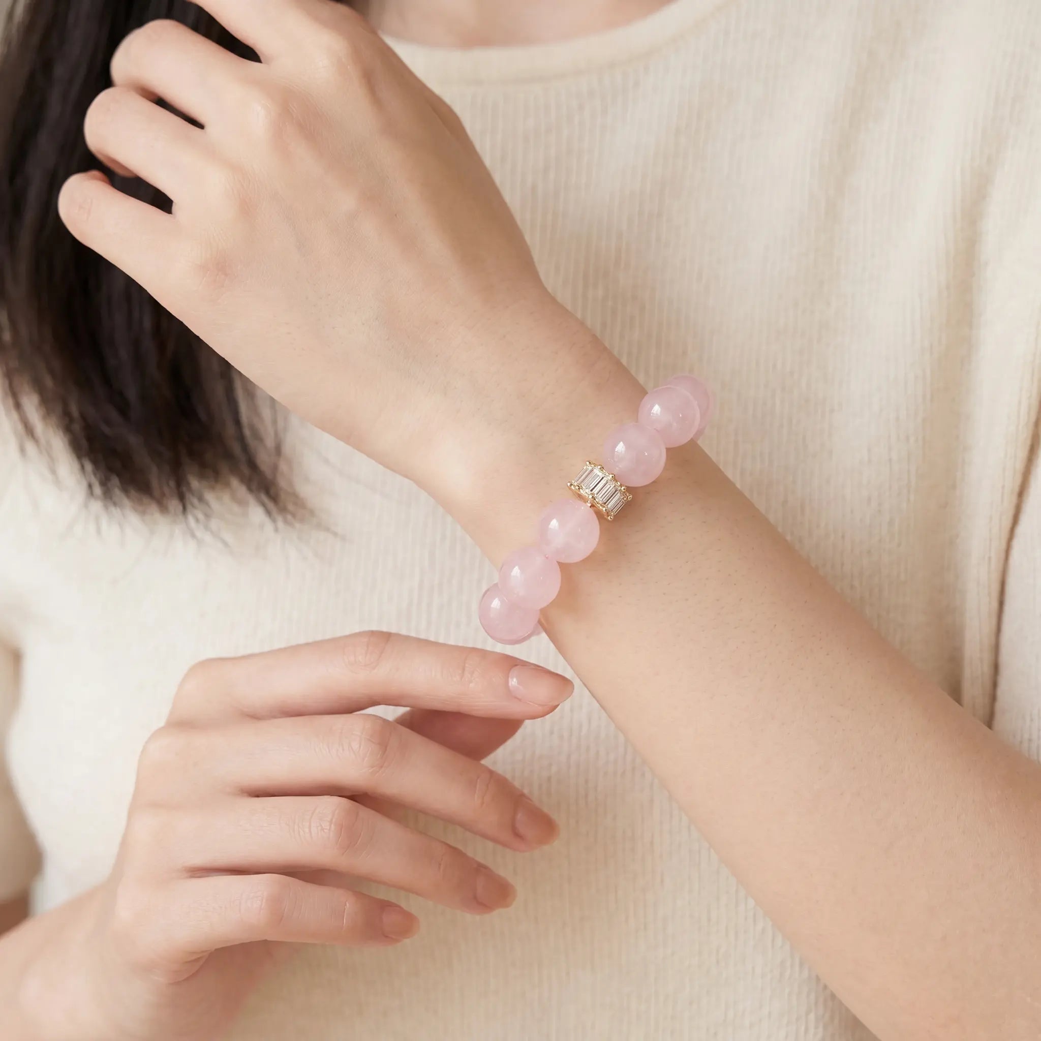 Front view portrait up to collarbone of a woman raising her left wrist with her right fingertips about to touch the crystal bracelet.