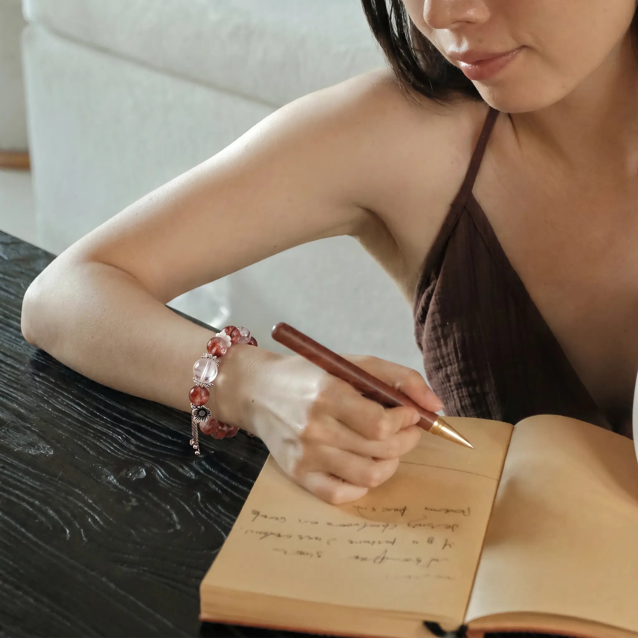 Downward high-angle shot from the upper-left side showing a woman writing with a quartz bead bracelet on her right wrist.