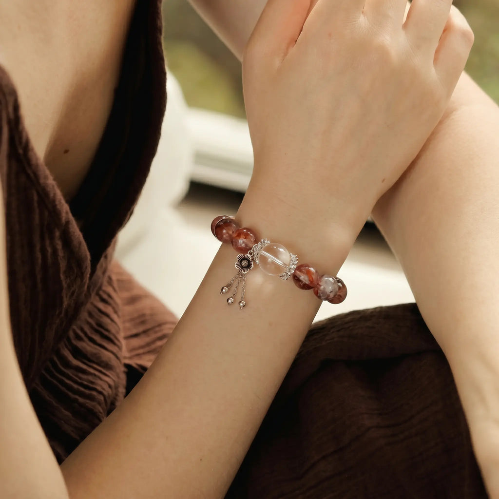 Right-side profile view of a seated woman gripping her left upper arm revealing a hematoid quartz bracelet.