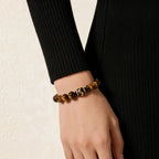 Side perspective view of a right hand resting flat over the hip side showcasing a luxury Tiger's eye cross-cultural bracelet.