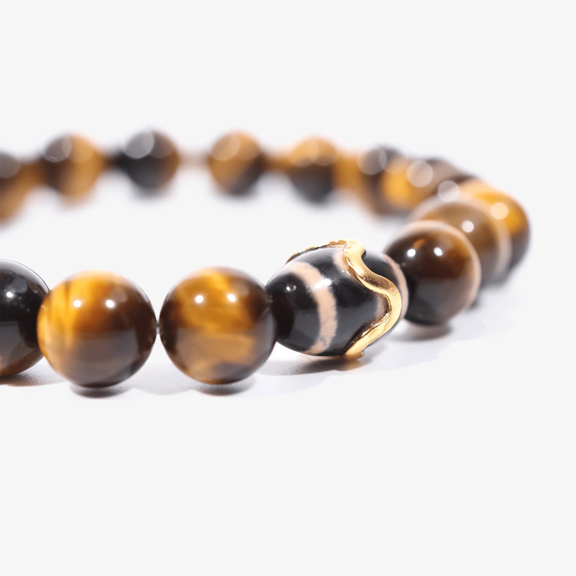 Cropped left-side half-view of the Kailash tiger's eye gemstone bracelet with a custom Dzi bead on white.