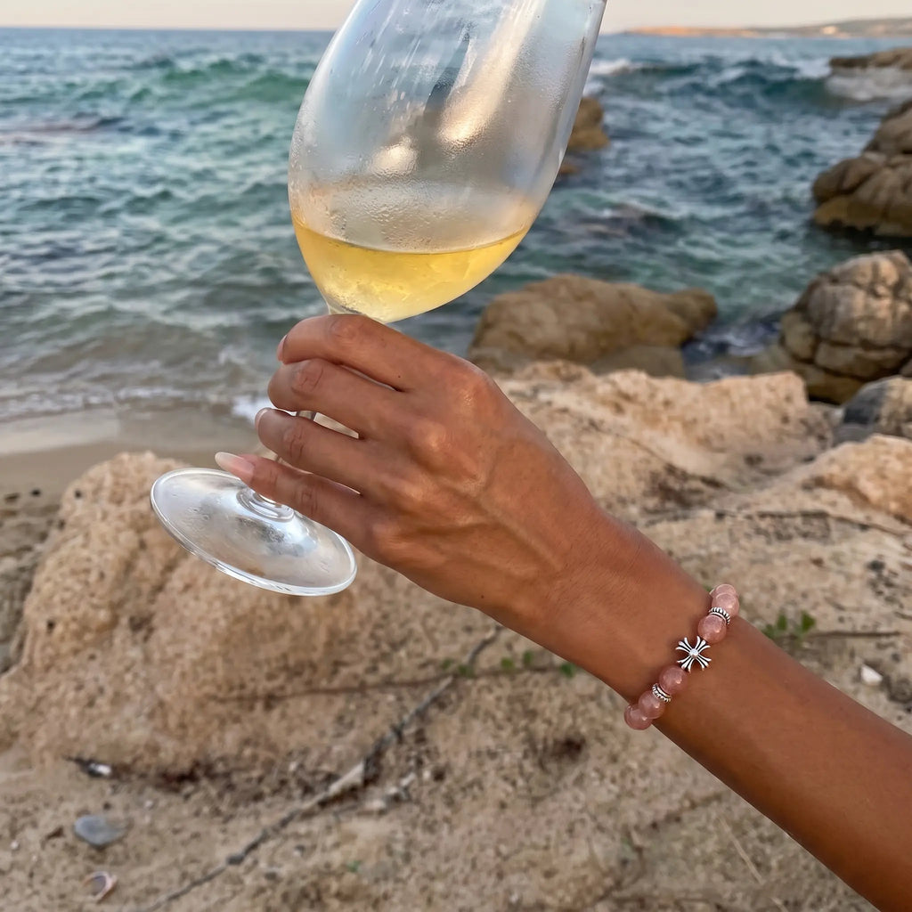 Close-up shot of a female left hand holding a luxury wine glass elegant stemware revealing the rhodochrosite beaded bracelet.