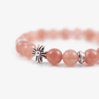 Close-up shot of a female left hand holding a luxury wine glass elegant stemware revealing the rhodochrosite beaded bracelet.