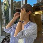 Profile view of a lady adjusting her retro sunglasses with both hands showcasing the crystal cross bracelet on her left wrist.