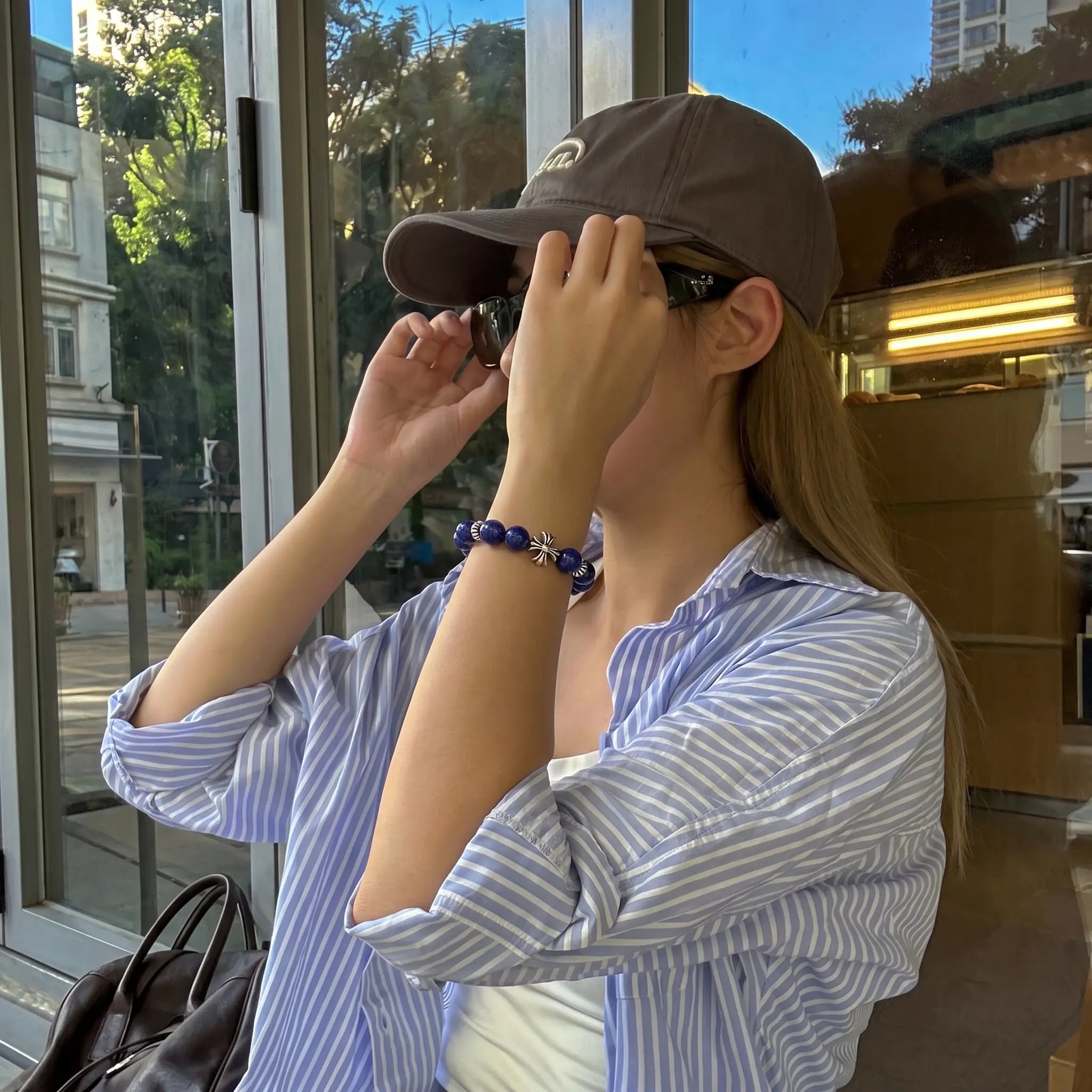 Profile view of a lady adjusting her retro sunglasses with both hands showcasing the crystal cross bracelet on her left wrist.