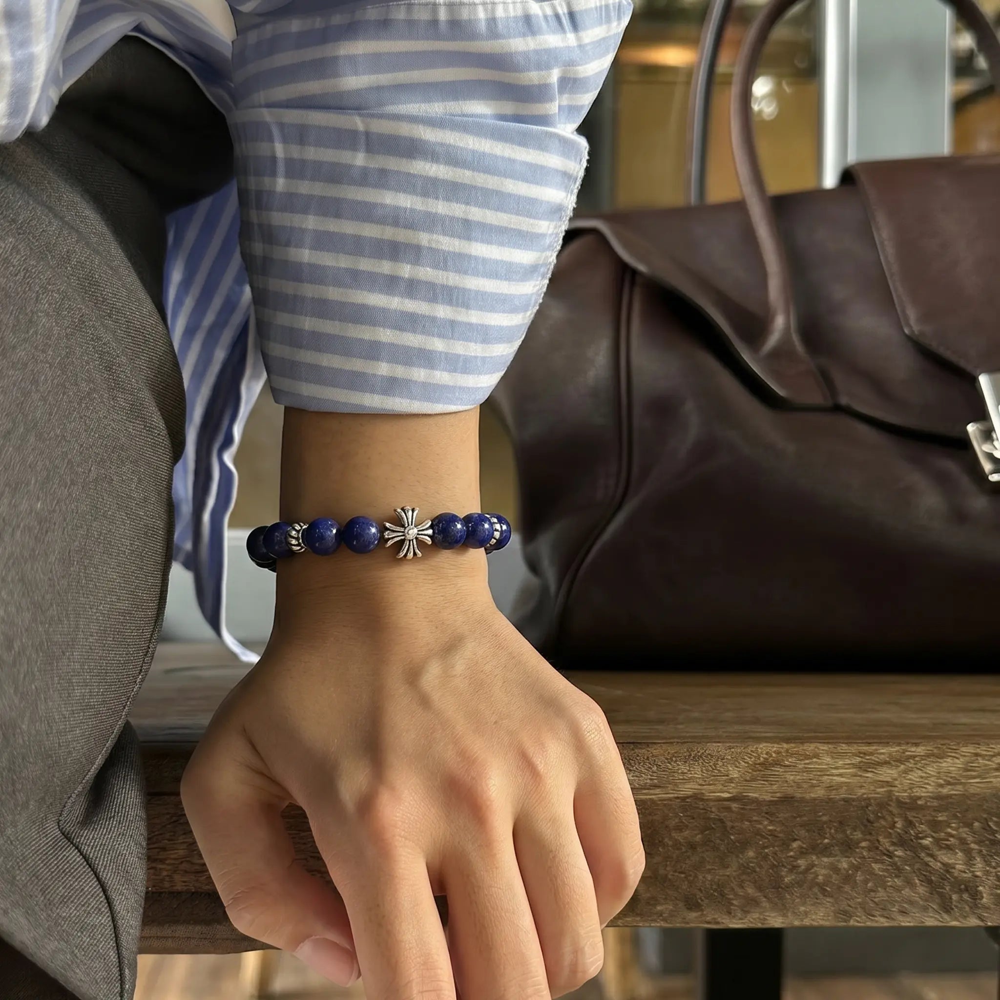 Close-up shot of a hand pressing down on a rustic wooden bench revealing a blue lapis lazuli bracelet on the wrist.