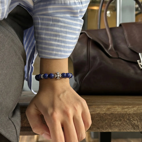 Close-up shot of a hand pressing down on a rustic wooden bench revealing a blue lapis lazuli bracelet on the wrist.
