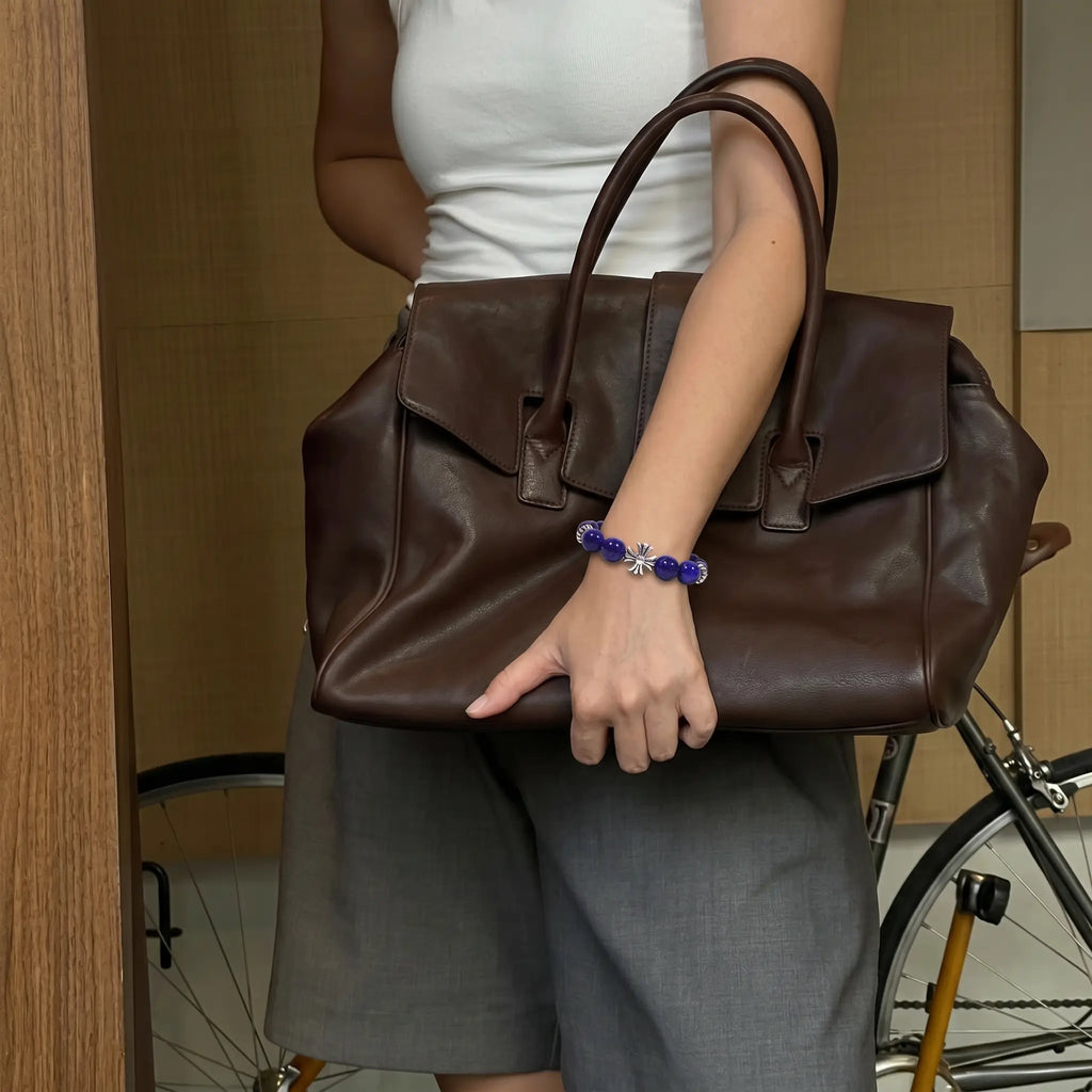 Front close-up shot of a female wrist holding a luxury designer leather handbag revealing a blue mineral crystal bracelet.